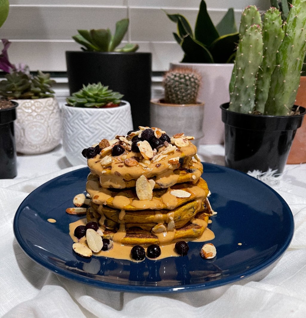 scrumptious vegan blueberry half stack of your dreams with a sweet pb drizzle topped with frozen blueberries and honey roasted almonds