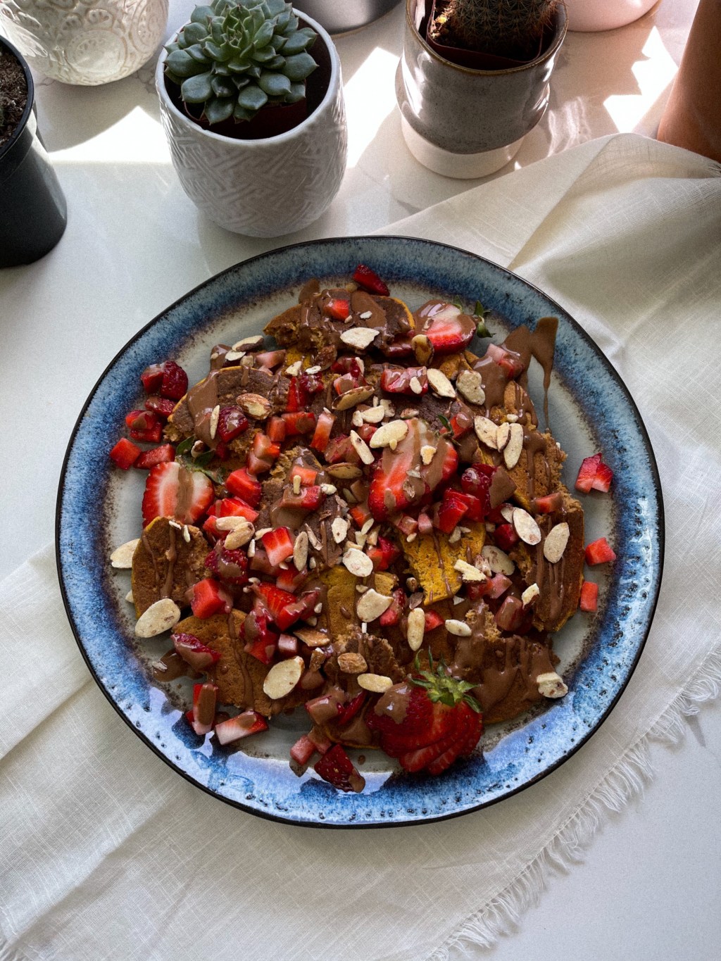 a beautiful plate stacked with tasty vegan strawberry cheesecake protein pancakes, fresh cut strawberries, honey roasted almond slices and a chocolate pb drizzle